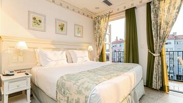 A hotel room with a large bed, two bedside tables, a window with curtains, and framed floral artwork on the wall.