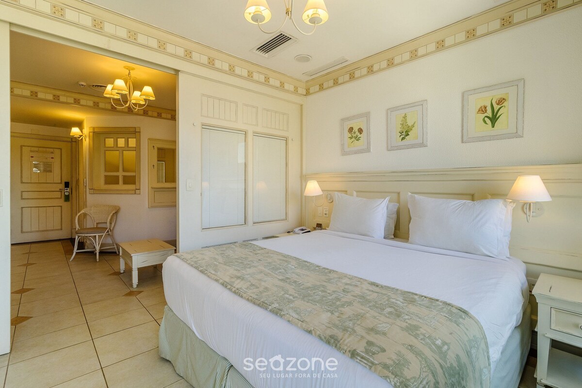 Una habitación de hotel con una cama grande, una silla, una mesita de noche y un tocador.