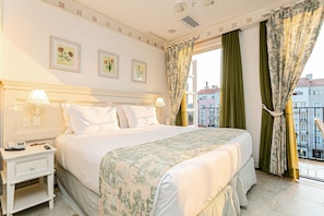 A hotel room with a large bed, two bedside tables, a window with curtains, and framed floral artwork on the wall.