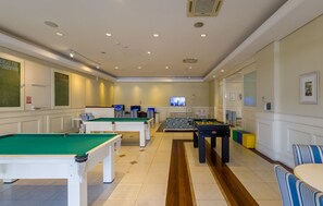 Una sala de billar con varias mesas de billar, un sofá y un televisor.