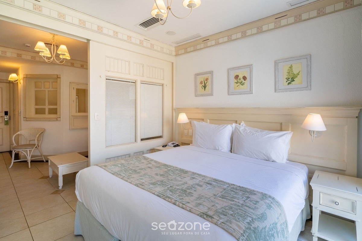 Una habitación de hotel con una cama grande, mesitas de noche, una silla y una ventana con contraventanas.