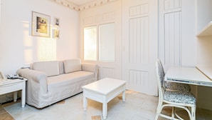 Una habitación con un sofá blanco, una pequeña mesa blanca, una silla blanca y un escritorio con una computadora.