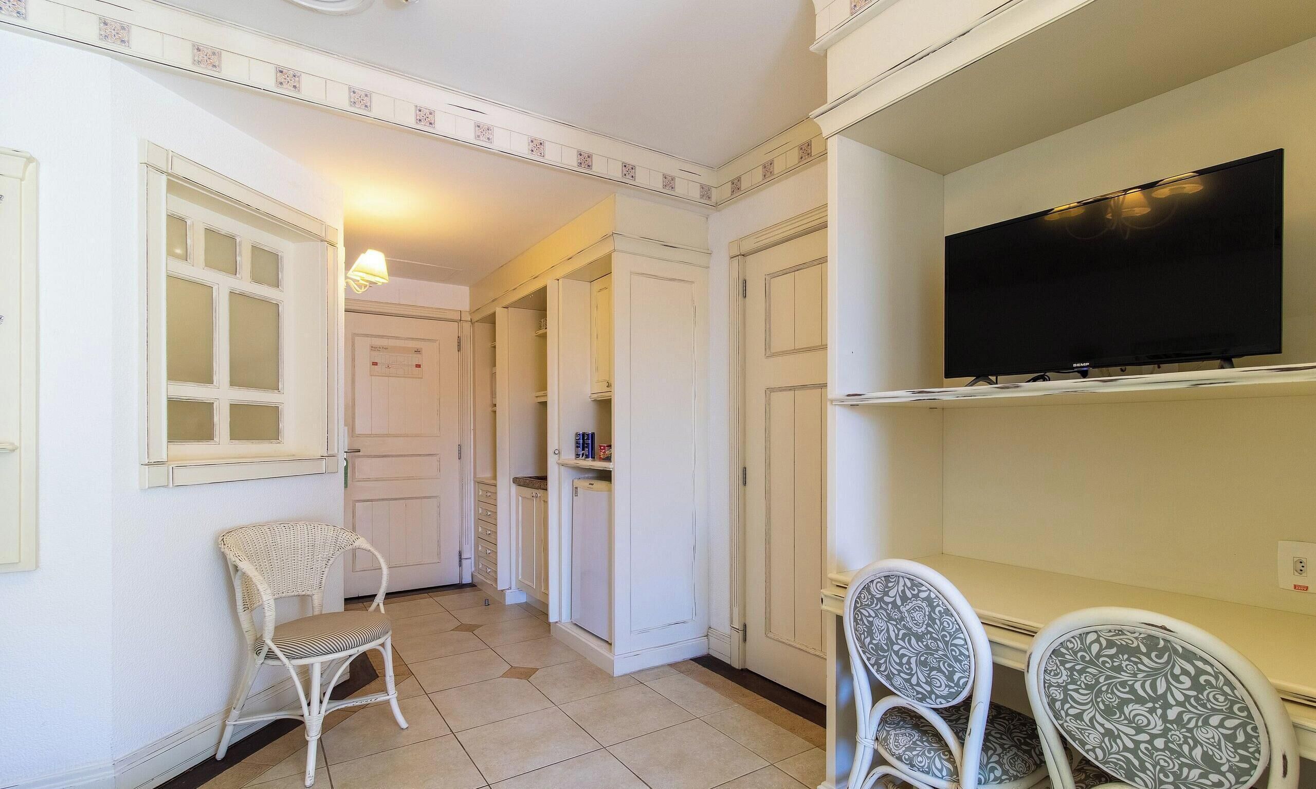 A hallway with a white chair, a small table, and a television on a stand.