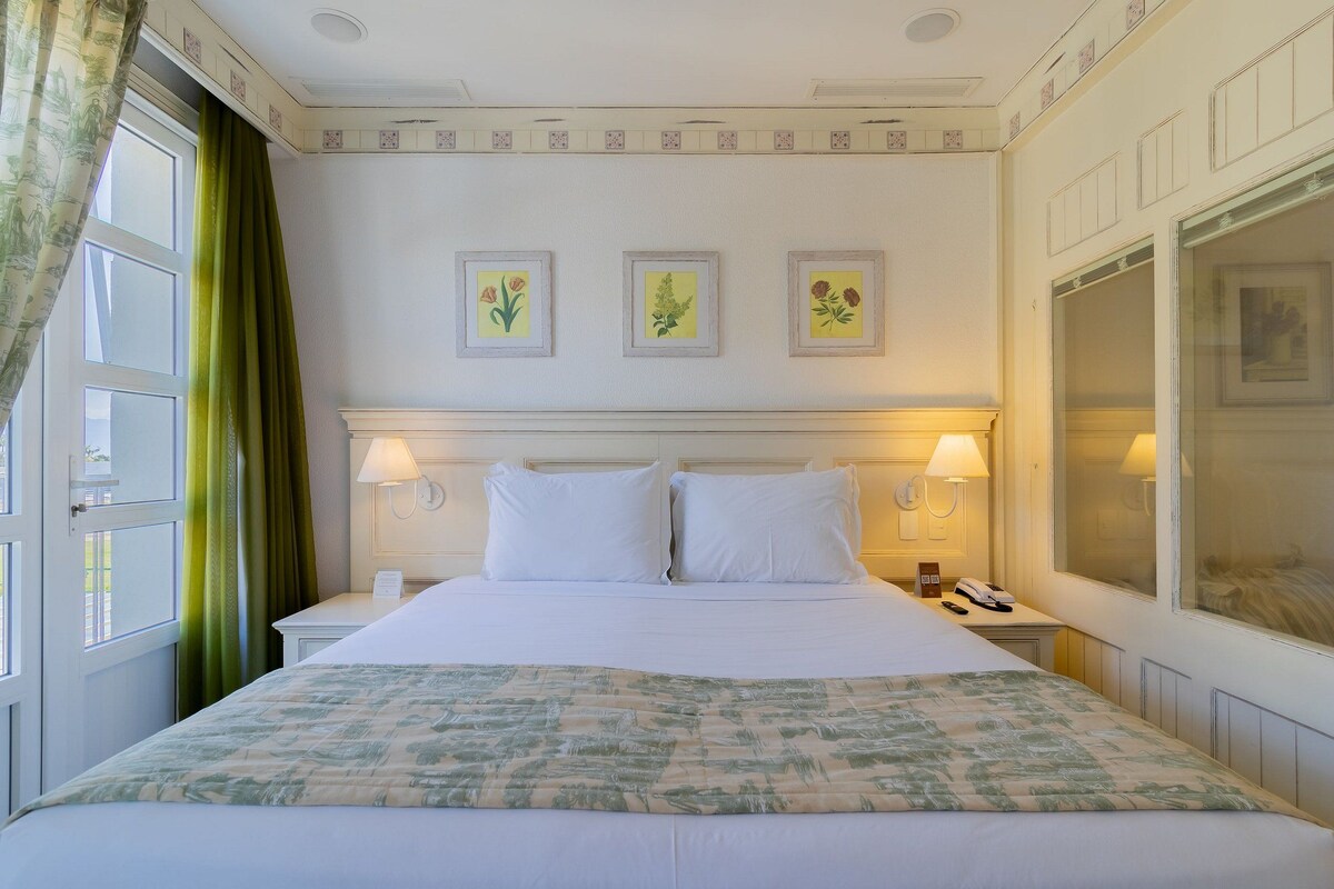 Una habitación de hotel con una cama grande, dos lámparas de noche, un teléfono y una ventana con cortinas.