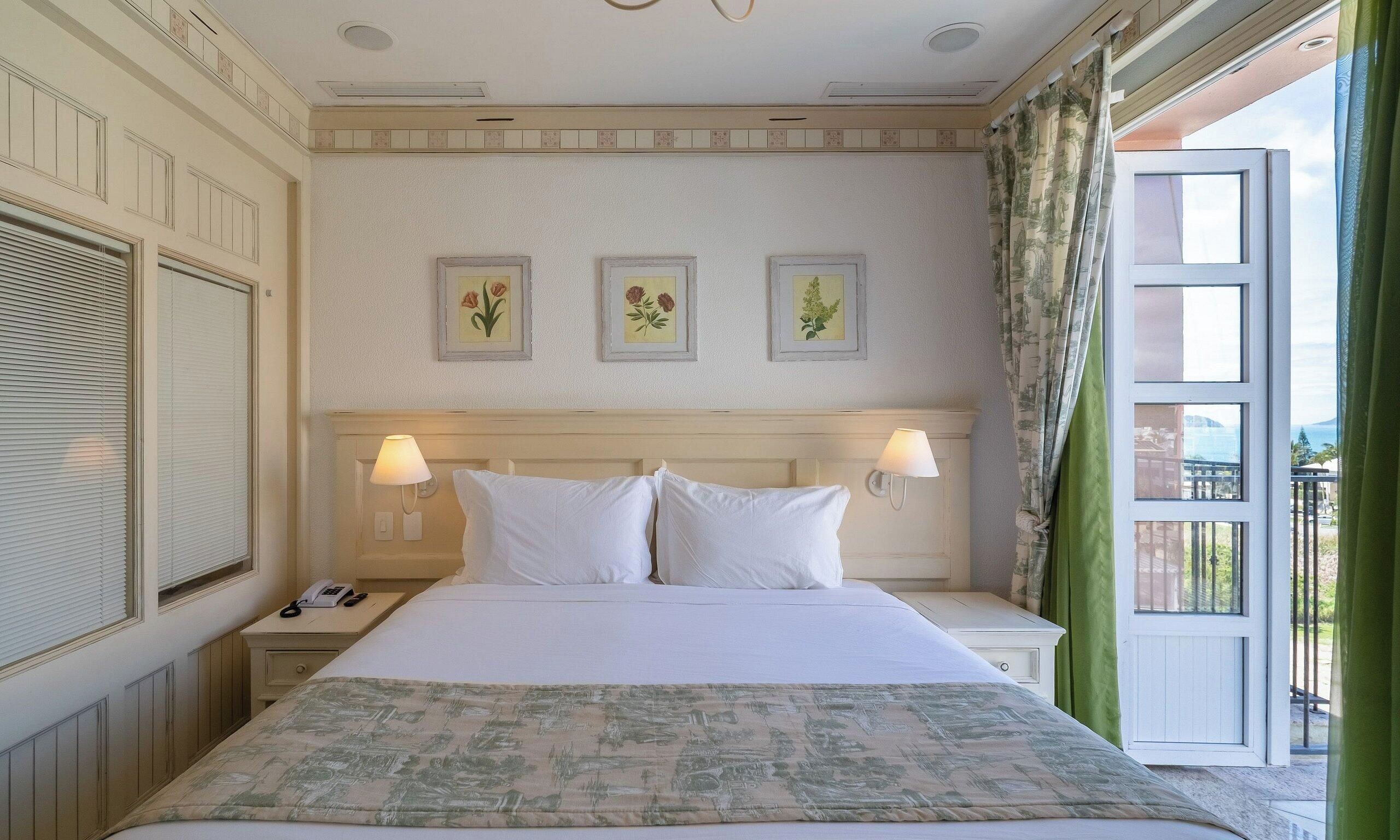 A hotel room with a bed, two bedside lamps, a telephone, and three framed botanical prints on the wall.