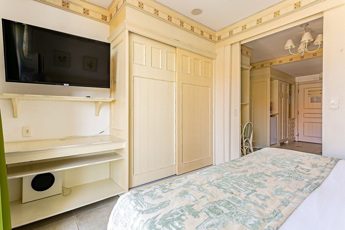 Un dormitorio con cama, televisor, armario y espejo.