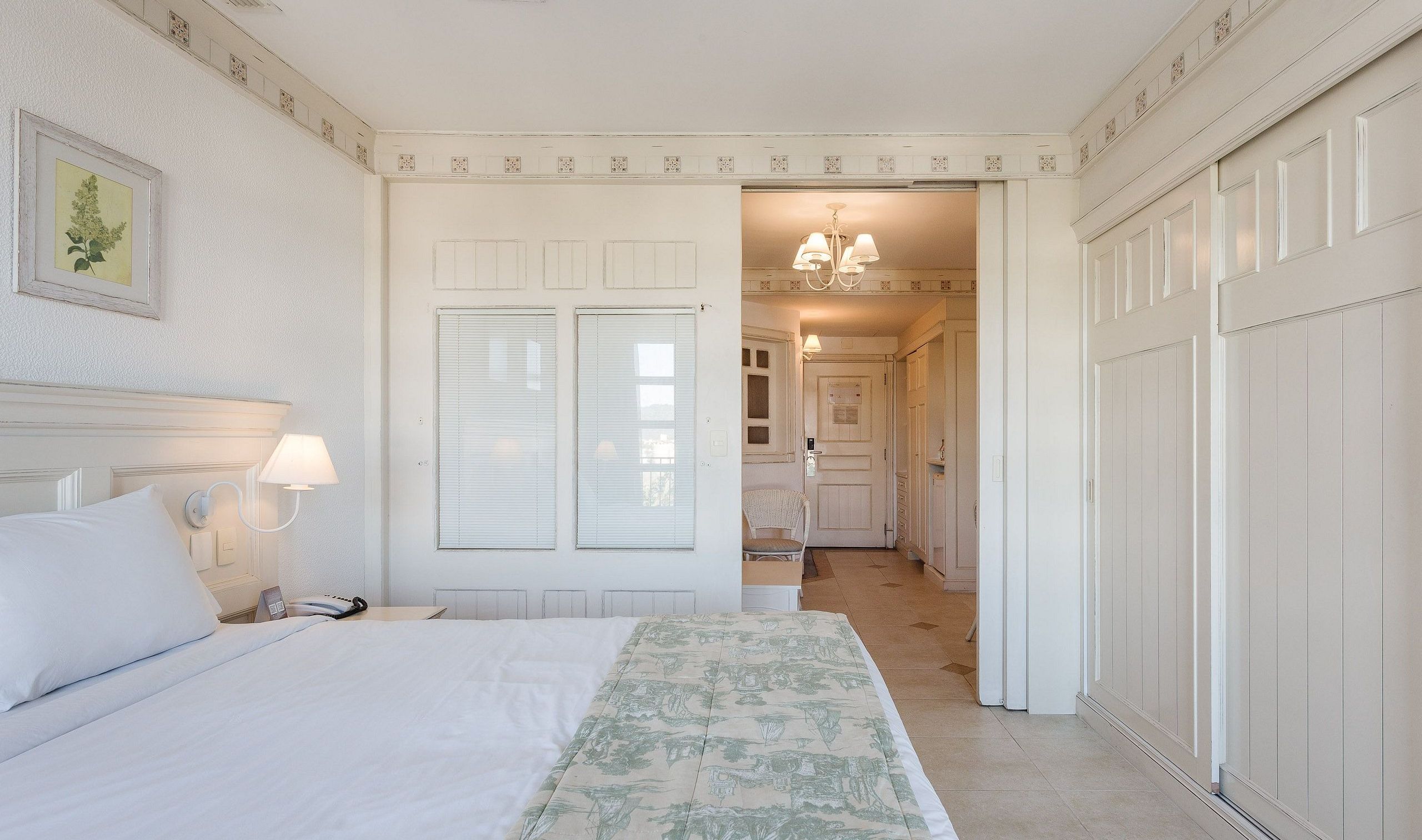 A hotel room with a bed, bedside lamps, a chair, a desk, and a bathroom visible through an open door.