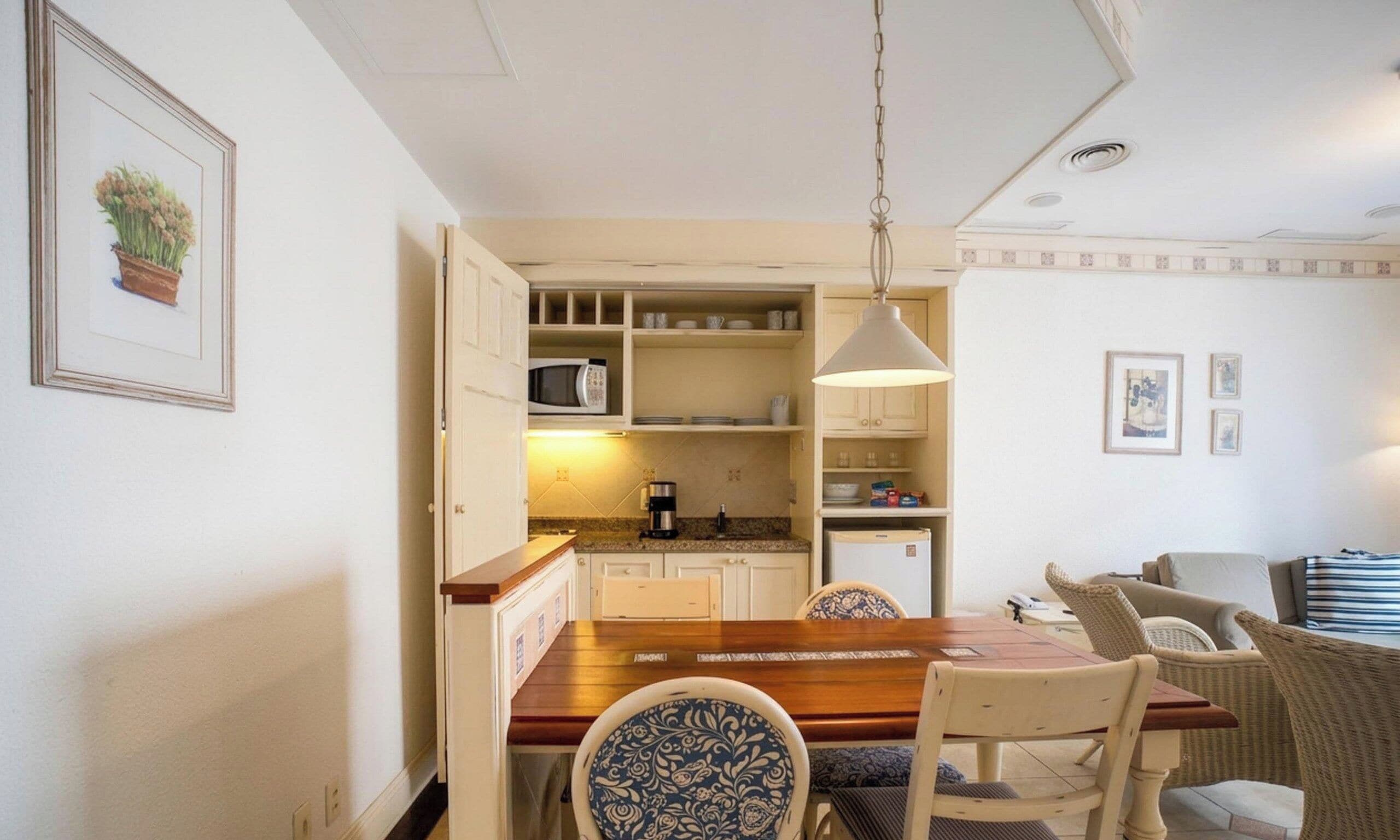 Cocina compacta con zona de comedor, que incluye una mesa de madera, sillas, una lámpara colgante y un refrigerador.