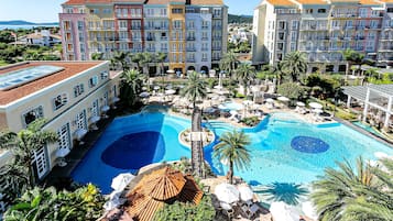 Een resort met een groot zwembad, meerdere gebouwen en palmbomen.