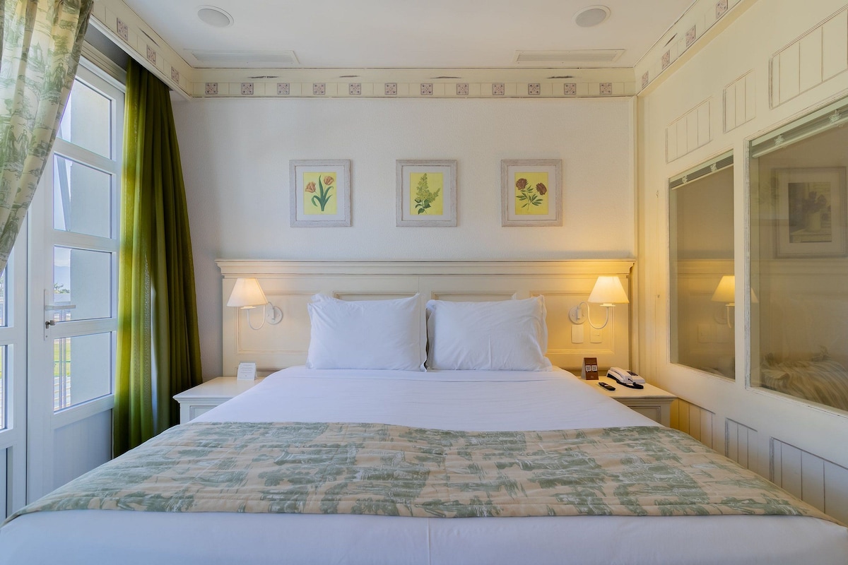 Una habitación de hotel con una cama grande, dos lámparas de noche, un teléfono y una ventana con cortinas.