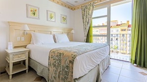 Habitación de hotel con cama, mesita de noche y ventana con vista a edificios.