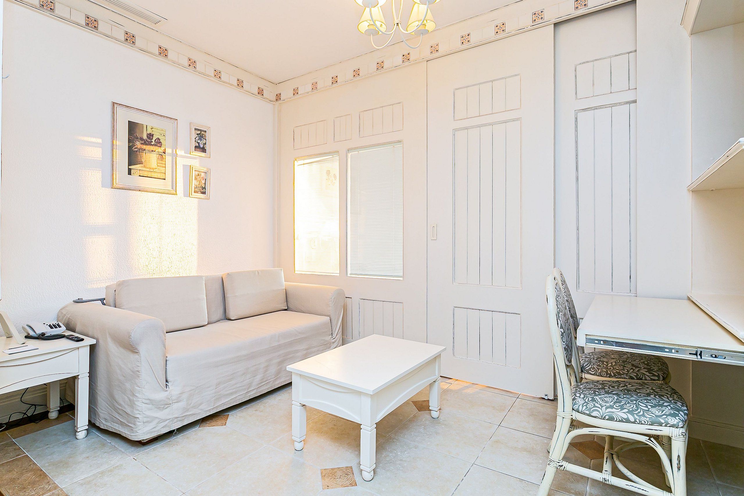 Una habitación con un sofá blanco, una pequeña mesa blanca, una silla blanca y un escritorio con una computadora.