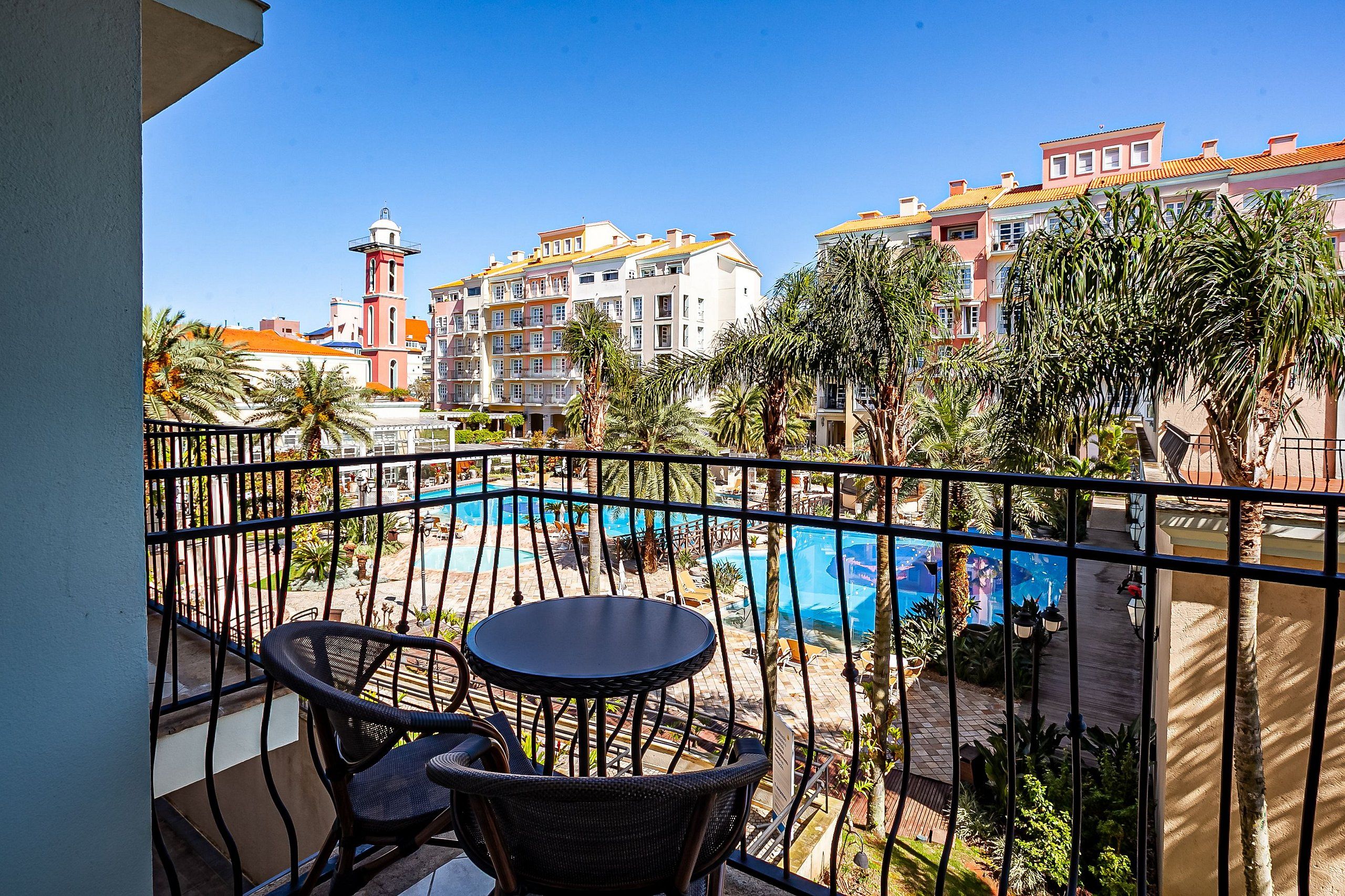 Ein Balkon mit Blick auf einen Swimmingpool, Palmen und Gebäude im Hintergrund.