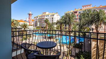 A balcony with a view of a swimming pool, palm trees, and buildings in the background.