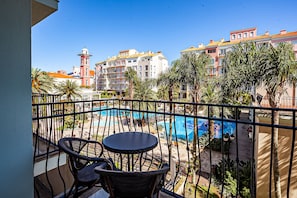 A balcony with a view of a swimming pool, palm trees, and buildings in the background. - Confortáveis Studios no IL Campanario Resort ILCJR (Florianópolis)