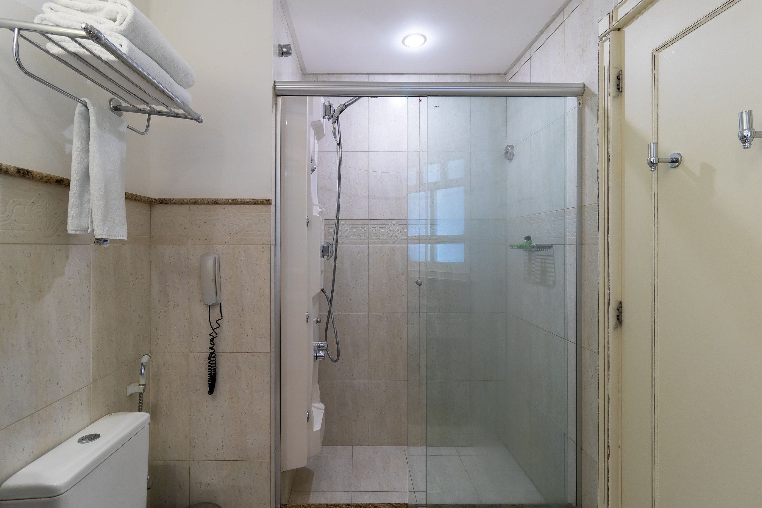 Chuveiro com porta de vidro, vaso sanitário e porta-toalhas com toalhas.