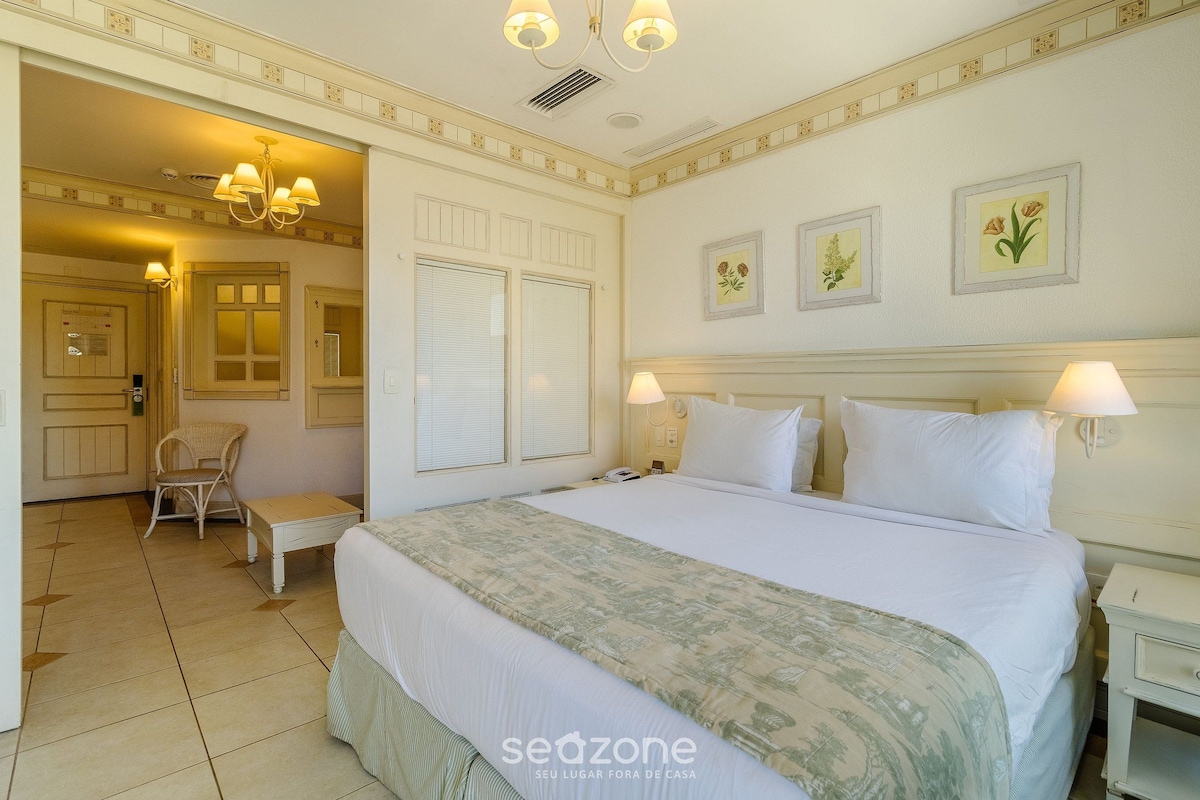 A hotel room with a large bed, a chair, a bedside table, and a nightstand.