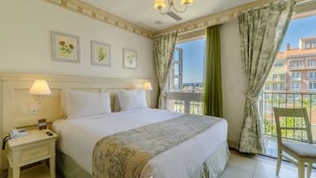 A hotel room with a bed, bedside lamps, a nightstand, a chair, a window with curtains, and a balcony view.