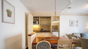 Une cuisine compacte avec un coin repas, comprenant une table en bois, des chaises, un luminaire suspendu et un réfrigérateur.