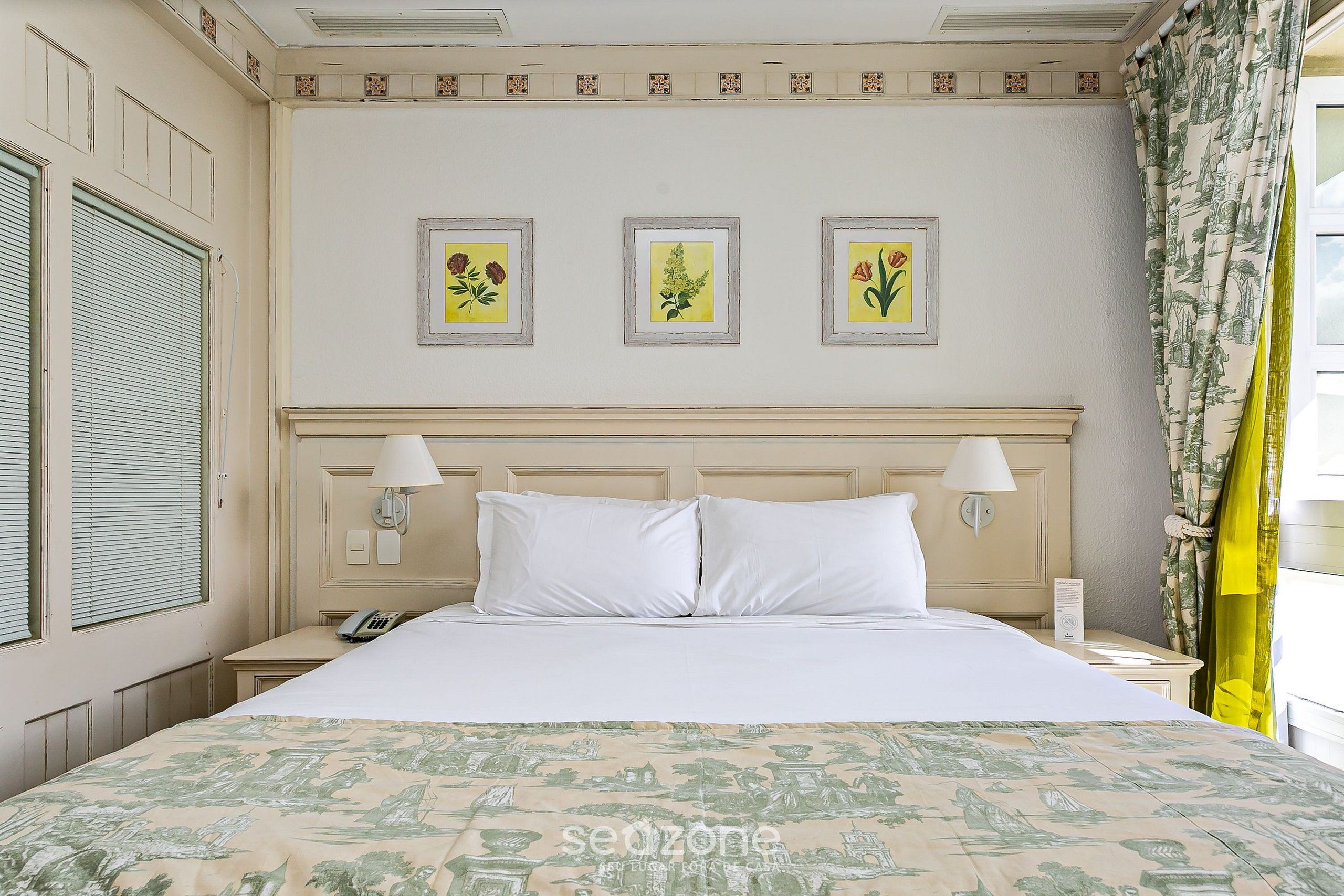 A hotel room with a bed, a nightstand, a telephone, and three framed pictures on the wall.