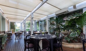 An outdoor dining area with tables and chairs, covered by a canopy, and surrounded by greenery. - Confortáveis Studios no IL Campanario Resort ILCJR (Florianópolis)