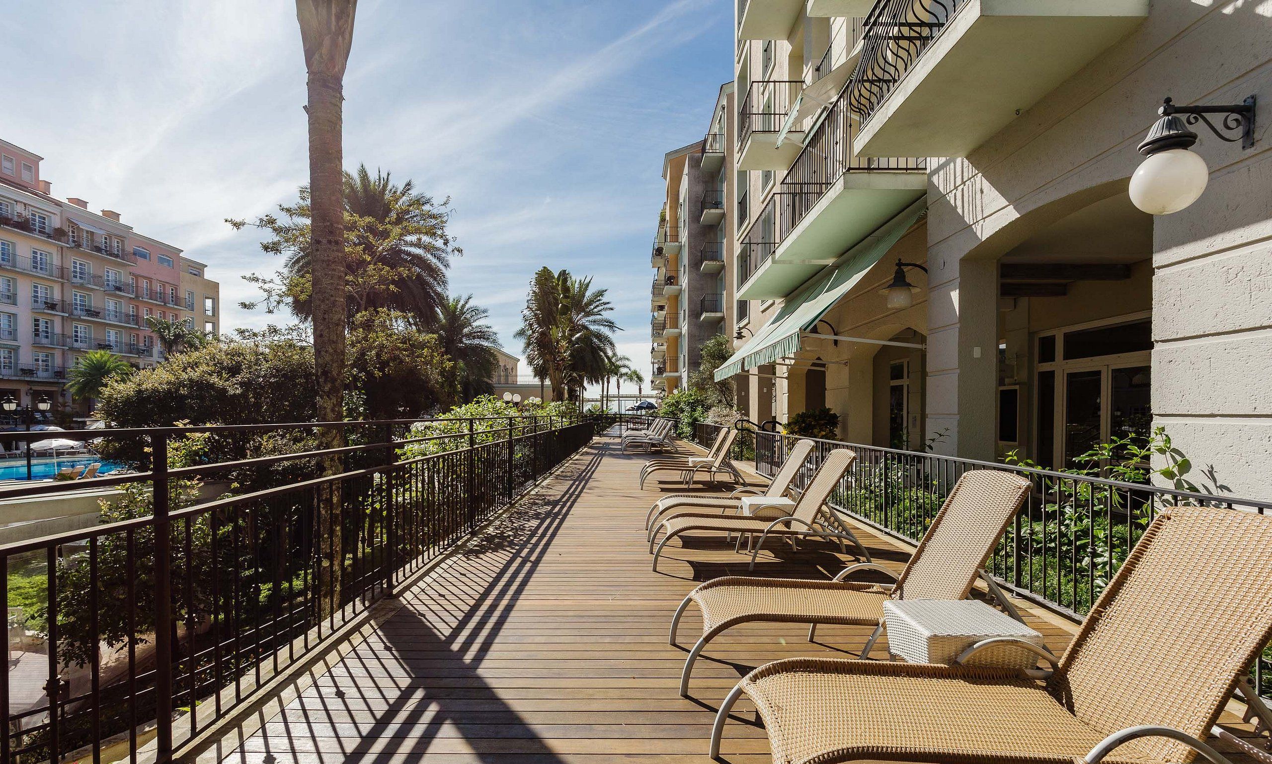A wooden deck with lounge chairs, a pool, and a row of buildings with balconies.