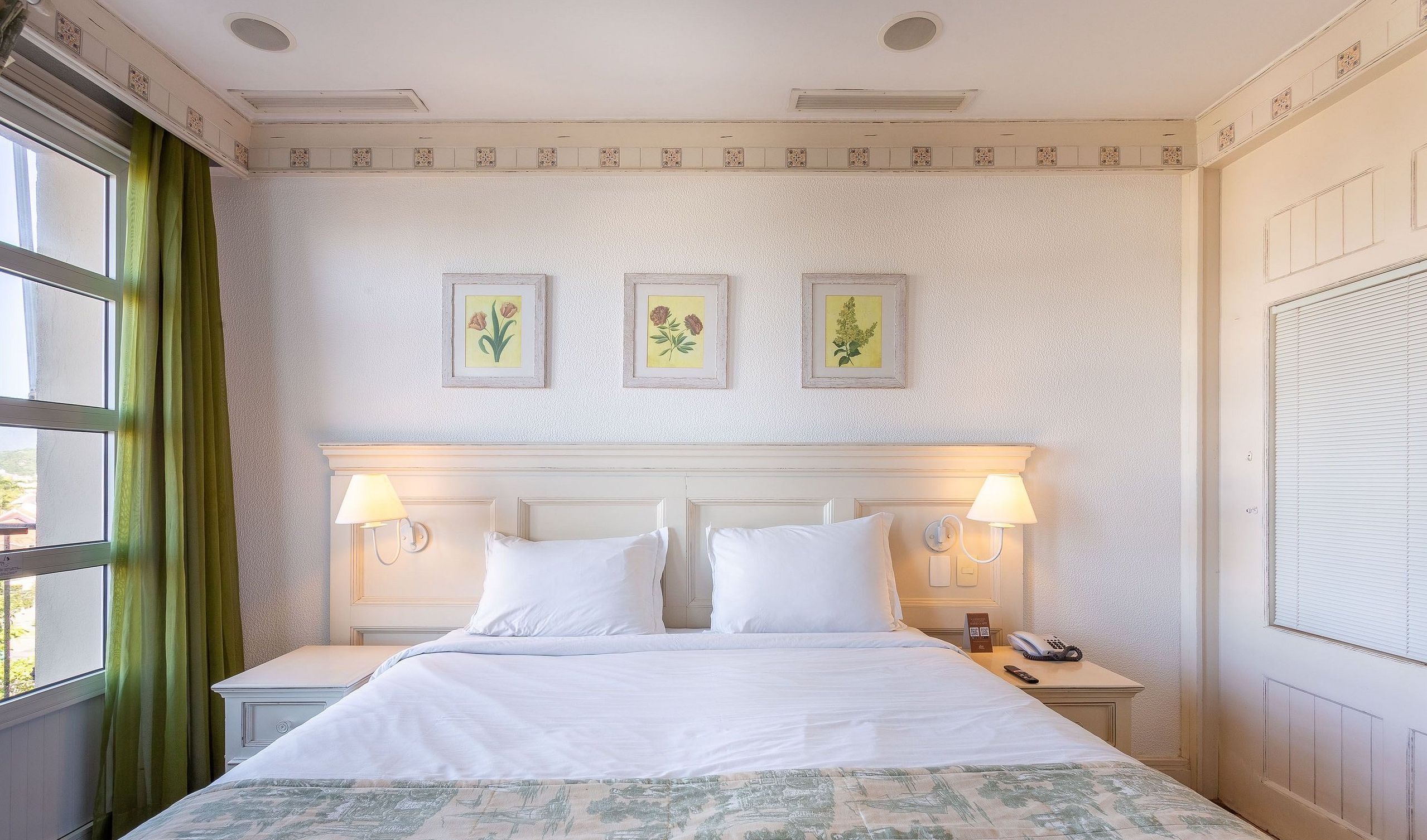 Quarto de hotel com uma cama grande, duas mesas de cabeceira e uma janela com cortinas.