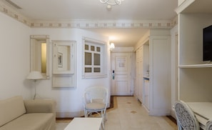 A room with a sofa, a chair, a table, a mirror, a door, and a television.