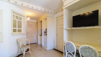 A hallway with a white chair, a small table, and a television mounted on the wall.
