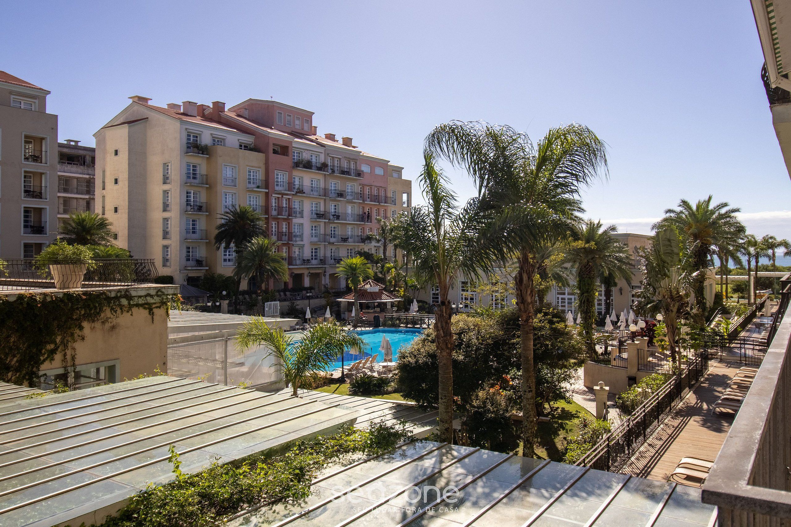 A hotel with multiple floors, a swimming pool, and palm trees.
