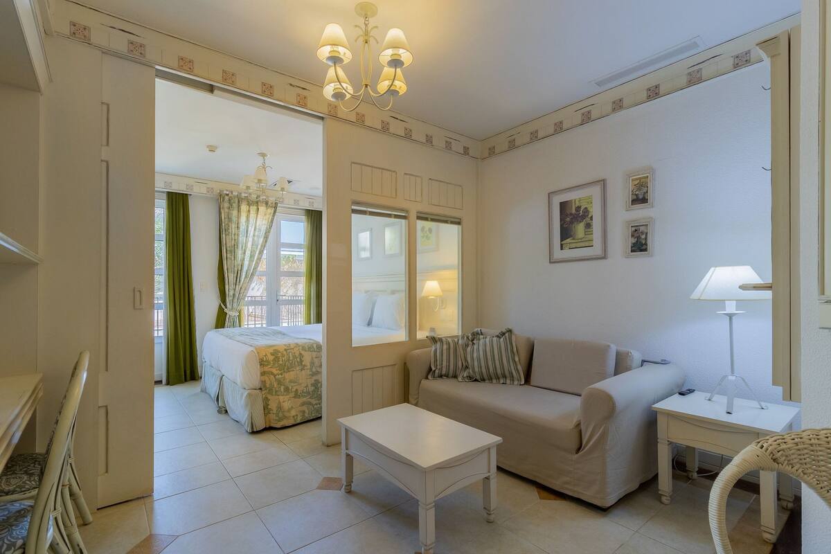 A room with a bed, a sofa, a table, a lamp, and a chair.