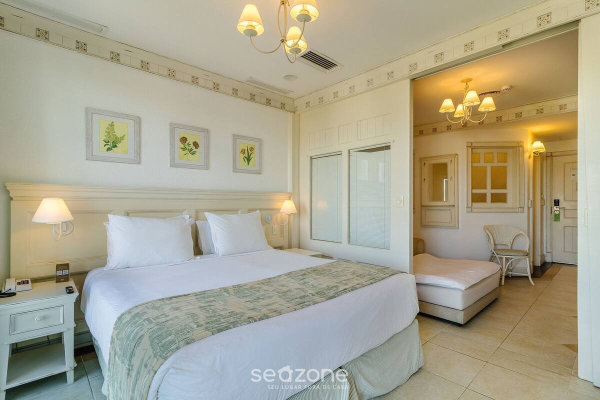 A hotel room with a large bed, two bedside tables, a chair, a desk, and a desk lamp.