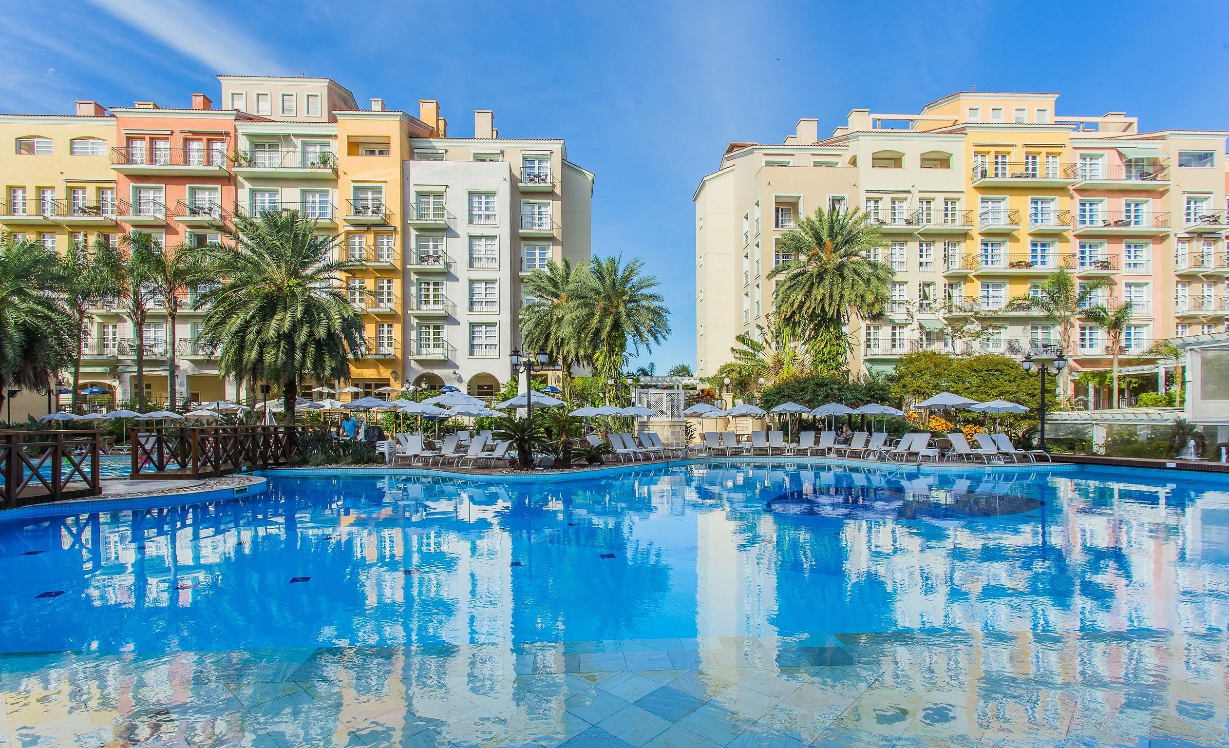 A swimming pool with lounge chairs and umbrellas, surrounded by multi-story buildings with balconies.