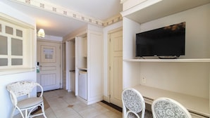 Una habitación con una televisión sobre un soporte, una silla y una puerta con un cartel.