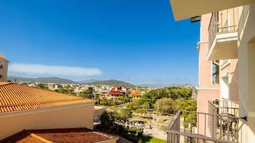 A balcony with a view of a residential area, including houses with red roofs and a mountain in the distance.