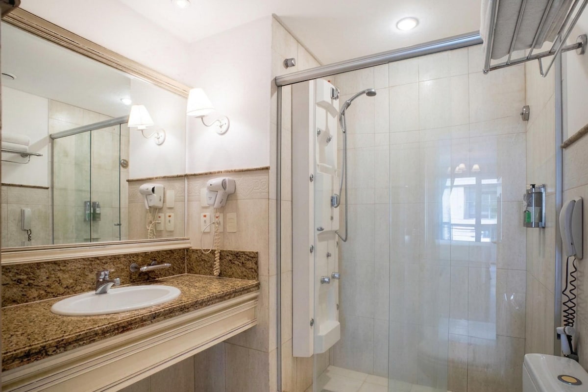 A bathroom with a granite countertop sink, a large mirror, and a glass-enclosed shower area.