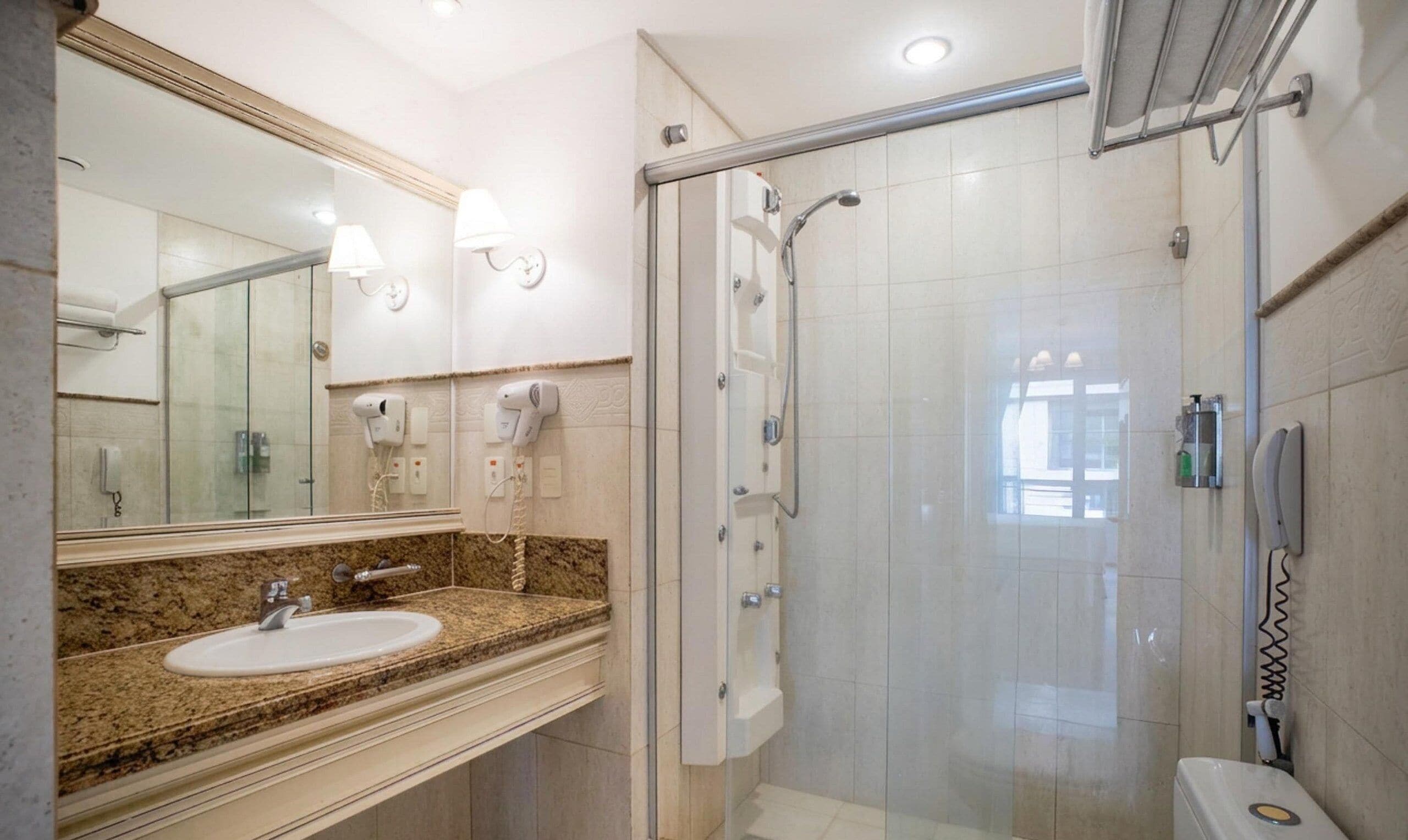 Baño con lavamanos de encimera de granito, un espejo grande y zona de ducha con mampara de vidrio.