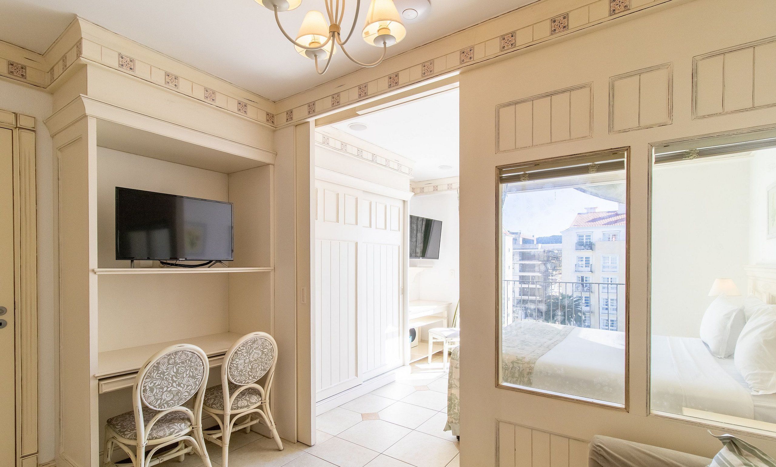 Una habitación con televisión en un estante, dos sillones estampados, una cama con vistas a edificios y un balcón.