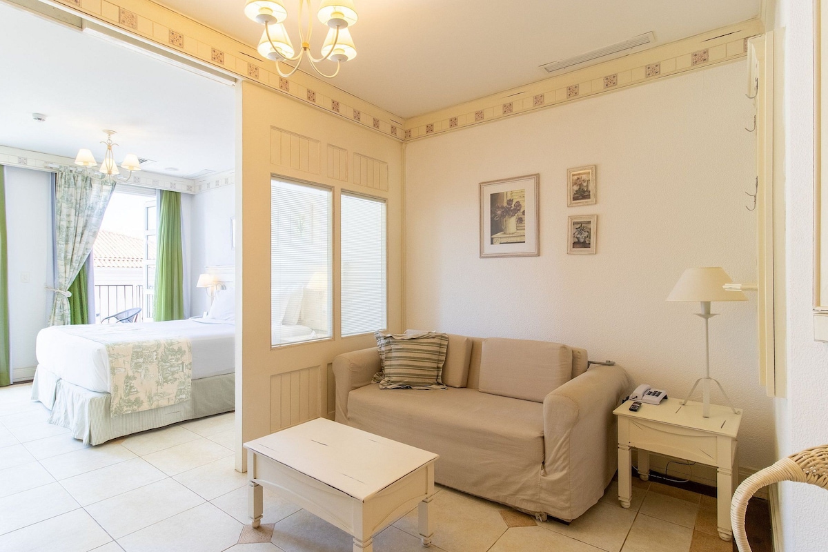 A hotel room with a bed, a sofa, a small table, a lamp, and a picture on the wall.
