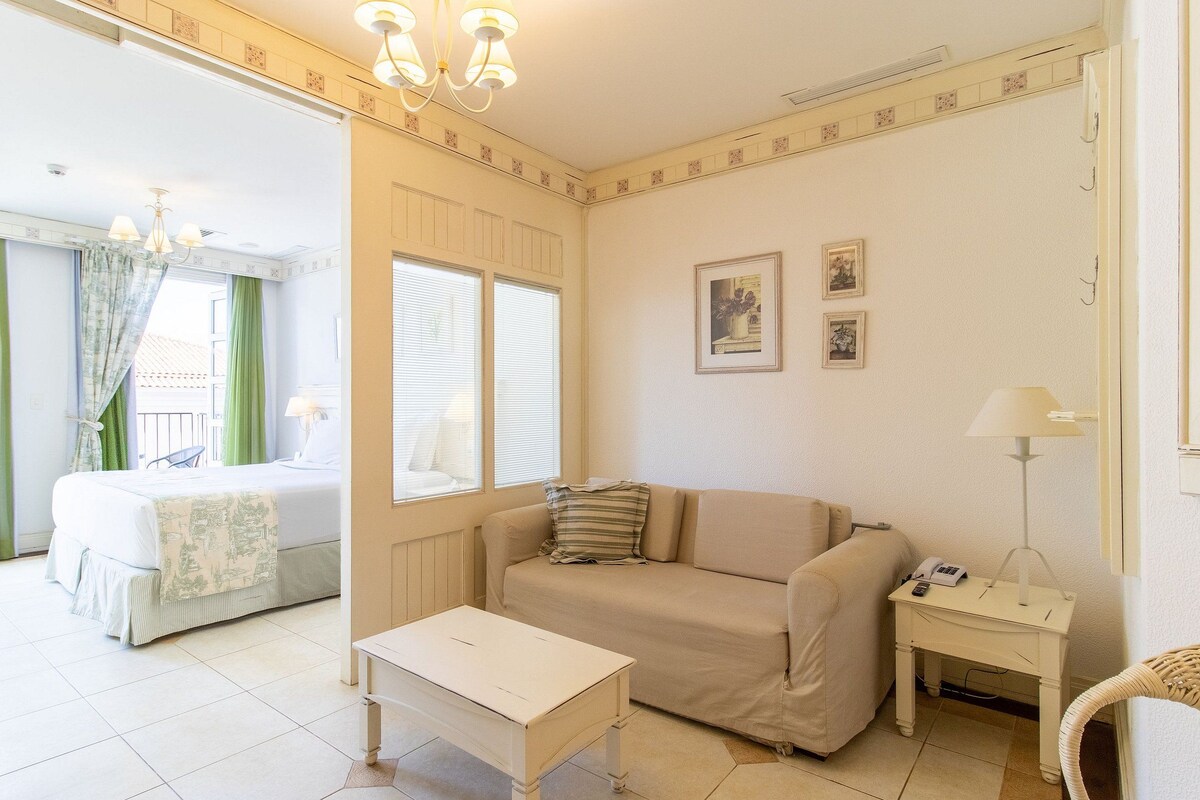 Una habitación de hotel con una cama, un sofá, una mesita, una lámpara y un cuadro en la pared.