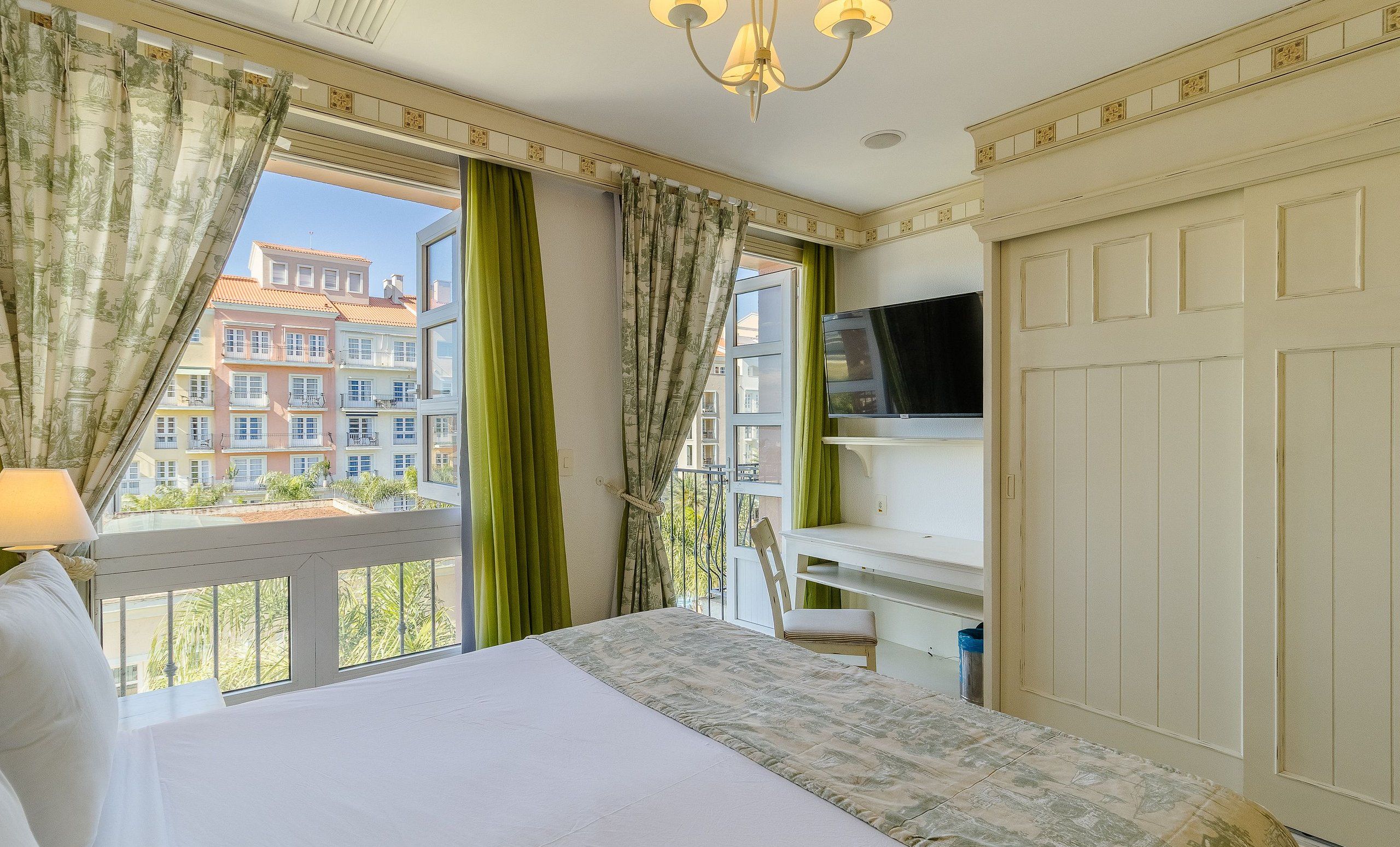 A hotel room with a bed, a TV, a desk, and a window with curtains.
