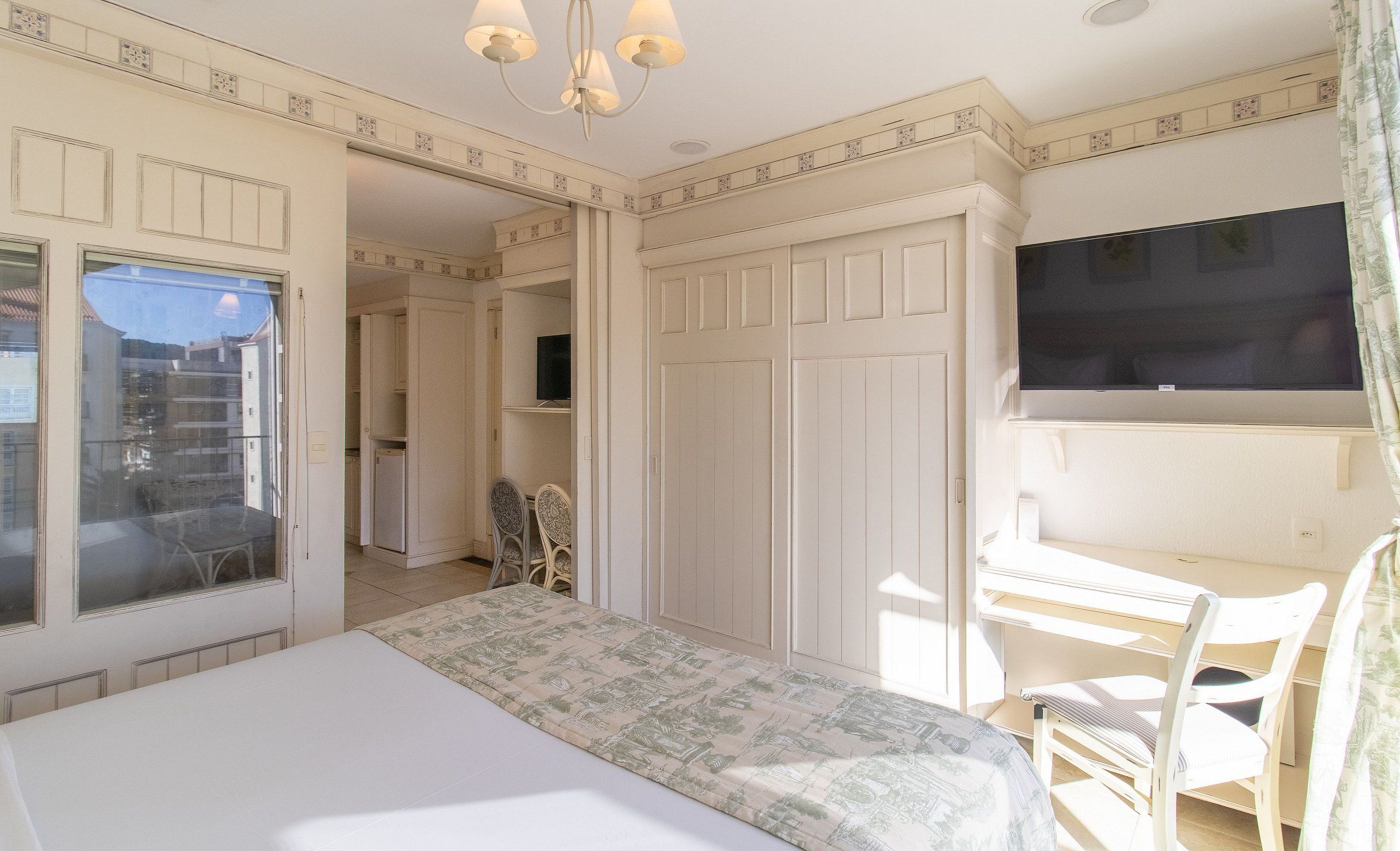A bedroom with a bed, a desk, a chair, a television, and a balcony.