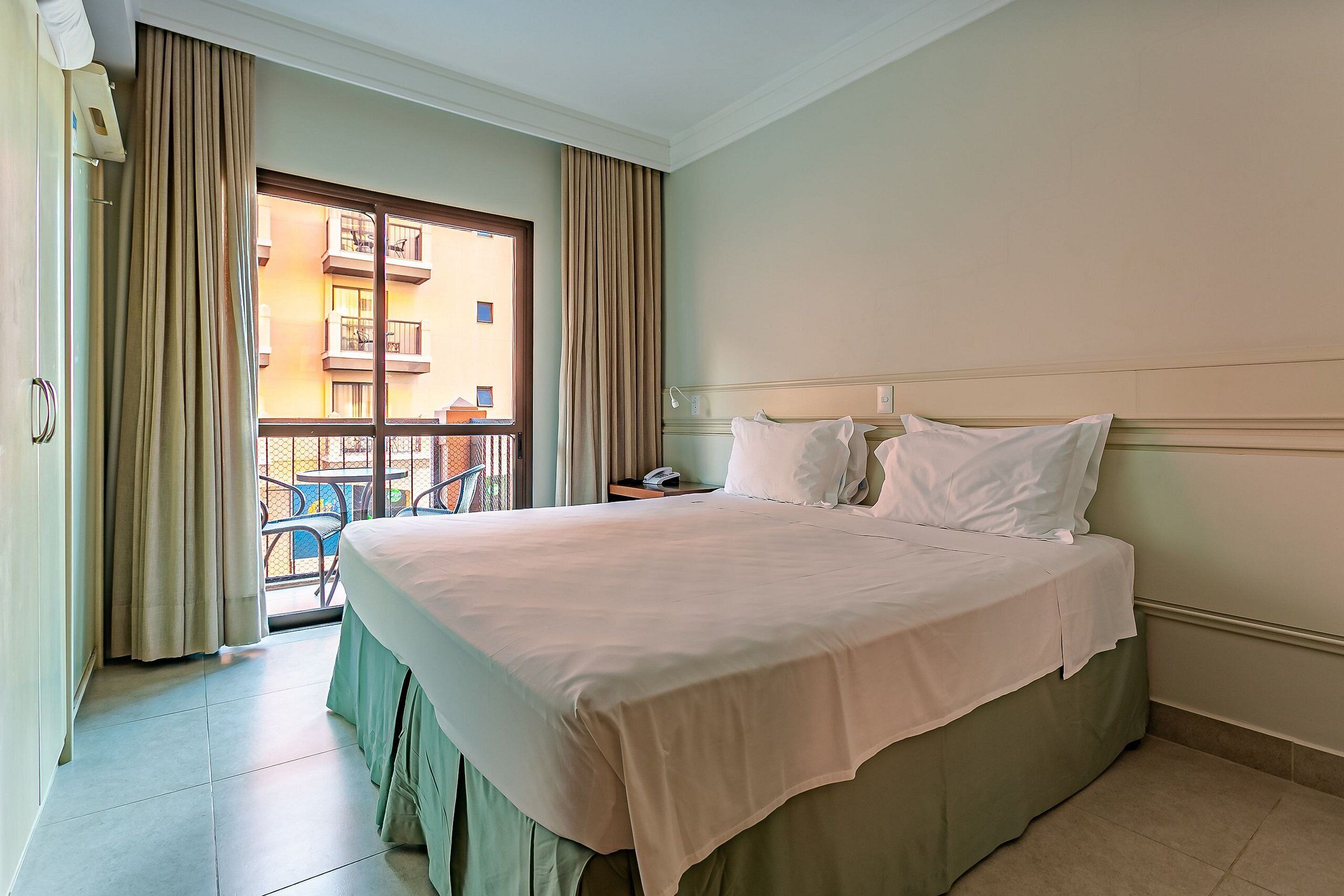 Habitación de hotel con una cama grande, una ventana con cortinas, un balcón y vistas a edificios.