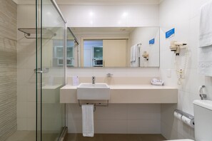 Un baño moderno con cabina de ducha de vidrio, un lavamanos blanco con toallero y un inodoro con dispensador de toallas de papel.