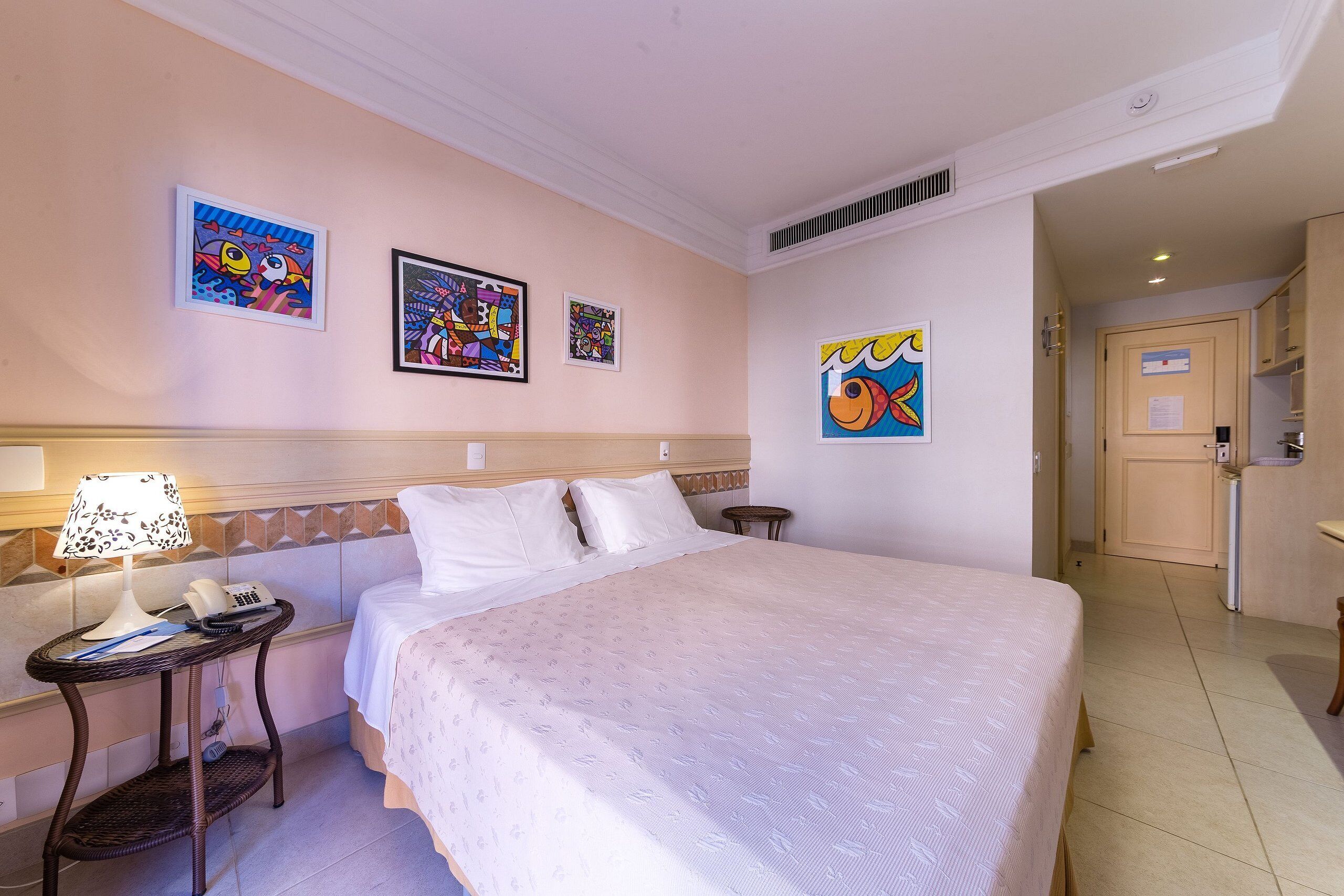 Una habitación de hotel con una cama grande, una mesita de noche con lámpara y obras de arte en las paredes.