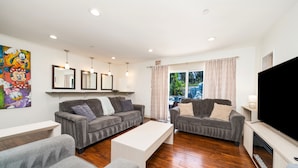 A living room with two grey sofas, a white coffee table, a flat-screen TV, and a fireplace. - Beautiful 5bd 3ba Private Resort Pool and HotTub, Waterslide, CloseTo Disneyland (Anaheim)