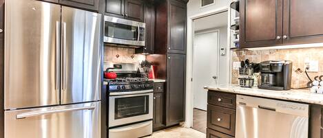 A modern kitchen with stainless steel appliances, dark wooden cabinets, and a tiled backsplash.