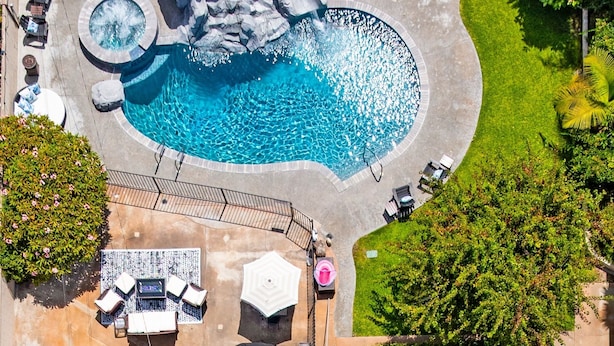 An aerial view of a swimming pool with a waterfall feature, surrounded by lounge chairs and a well-maintained lawn. - Beautiful 5bd 3ba Private Resort Pool and HotTub, Waterslide, CloseTo Disneyland (Anaheim)