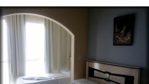 A hotel room with a bed, a window with curtains, and a painting on the wall.