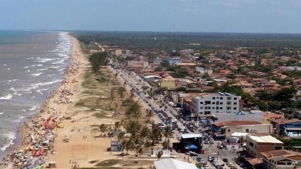 An aerial view of a beach with a densely populated area adjacent to it, featuring buildings and a road.